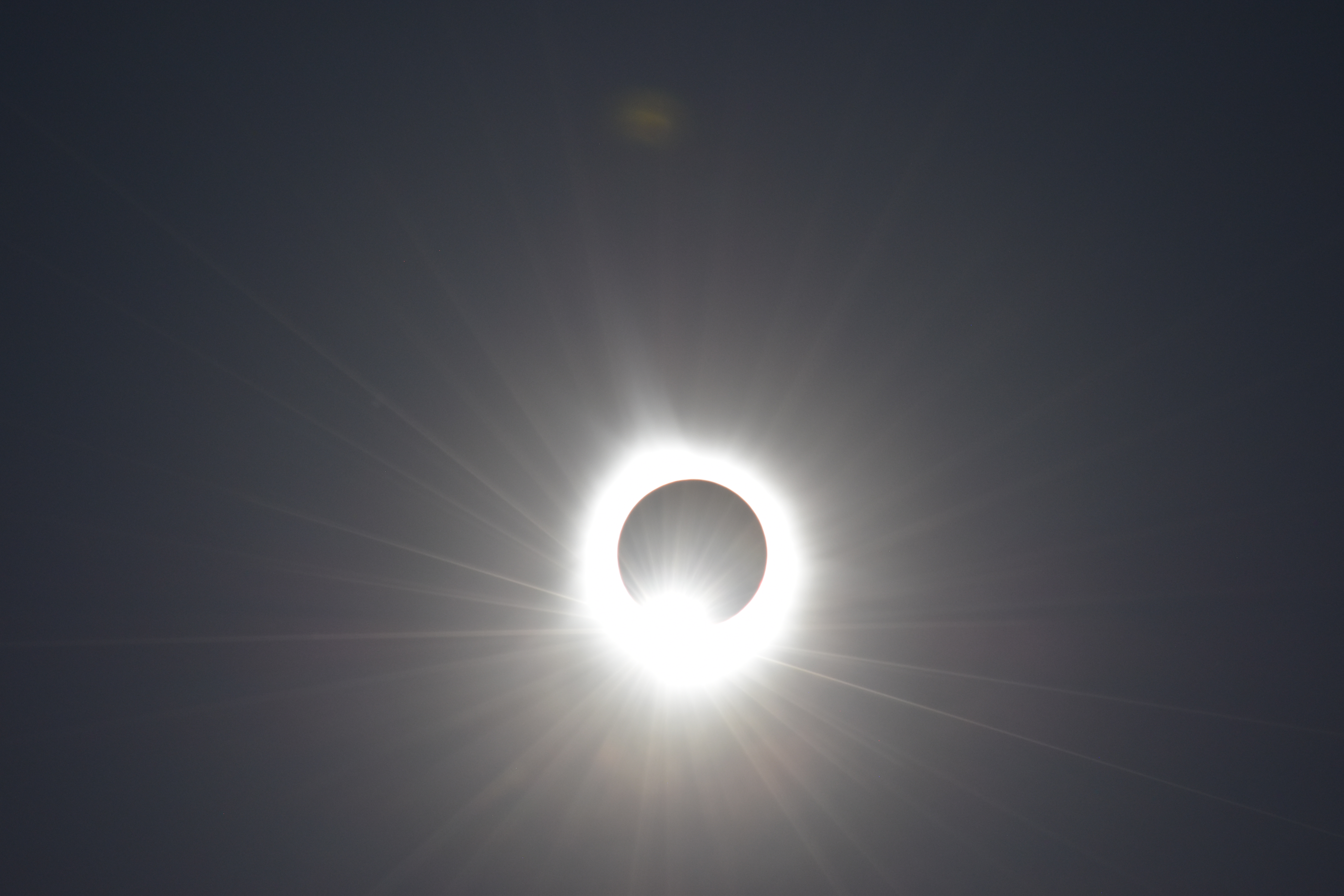 A digital photograph of a solar eclipse right on the edge of ending, sunlight leaking out around it